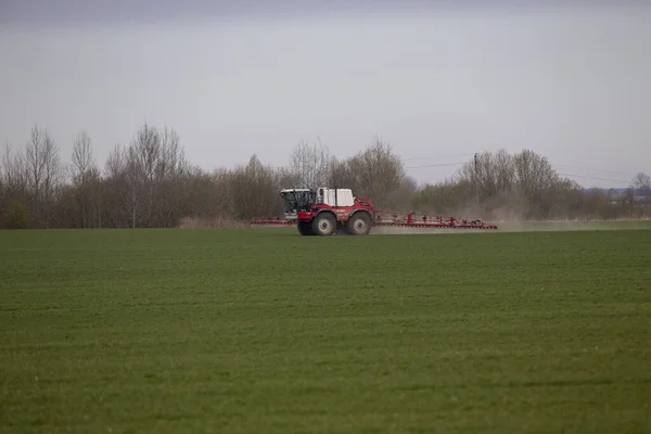 高い車輪のトラクターは 若い小麦に肥料を作っています 精巧に分散させたスプレー化学物質の使用 精巧に分散させた肥料のためのスプレー装置付けトラクター — ストック写真