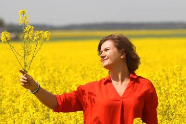 Kırmızı elbiseli mutlu bir genç kadın yaz mevsiminde tecavüz tarlasında eğleniyor. Petrol sahası olan kırsal bir arazi. Bahar çiçeği ve yağ.