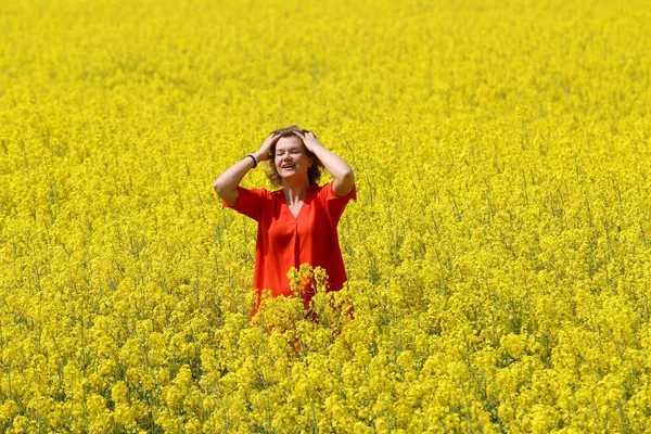 Kırmızı elbiseli mutlu bir genç kadın yaz mevsiminde tecavüz tarlasında eğleniyor. Petrol sahası olan kırsal bir arazi. Bahar çiçeği ve yağ.