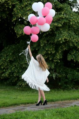 Genç ve güzel bir kız havada bir sürü renkli balon tutuyor.