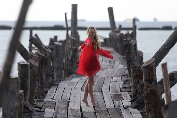 Kırmızılı güzel bir kız, deniz kenarındaki tahta bir köprüde poz veriyor. Özgürlük kavramı.