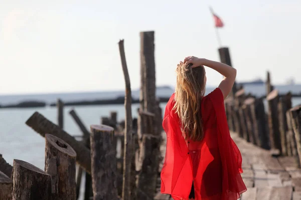 海のそばの木製の橋の上に赤の美しい少女がポーズをとっている フリードの概念 — ストック写真