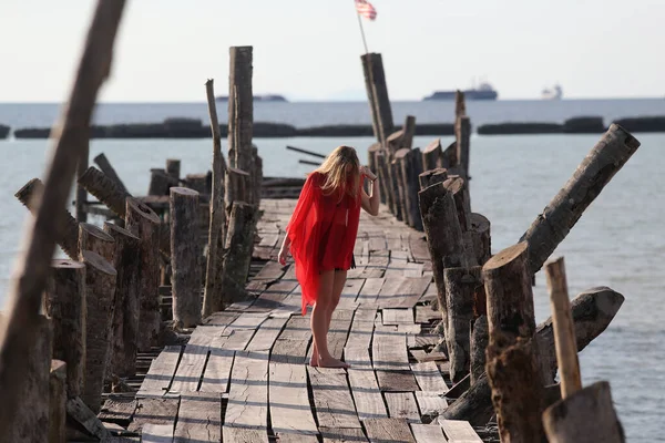 Kırmızılı güzel bir kız, deniz kenarındaki tahta bir köprüde poz veriyor. Özgürlük kavramı.