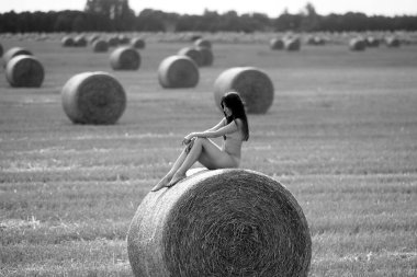 Genç bir kadın samanlıkta poz veriyor. Açık havada poz veren seksi esmer