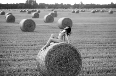 Genç bir kadın samanlıkta poz veriyor. Açık havada poz veren seksi esmer