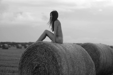 Genç bir kadın samanlıkta poz veriyor. Açık havada poz veren seksi esmer