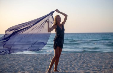 Bir kadın sahilde atkıyla poz veriyor.