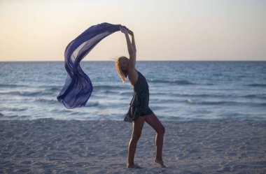 Bir kadın sahilde atkıyla poz veriyor.