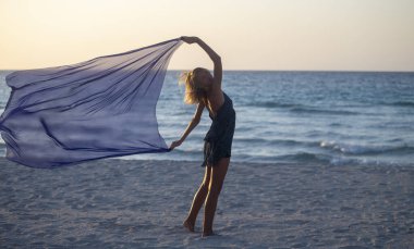 Bir kadın sahilde atkıyla poz veriyor.