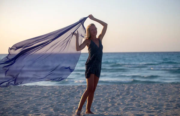 Bir kadın sahilde atkıyla poz veriyor.