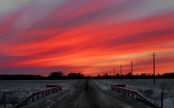 Beautiful colorful sunset winter landscape with a road to the village