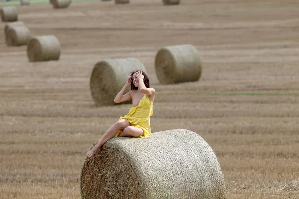 Young woman posing near haystack on the field. Sexy brunette posing outdoors