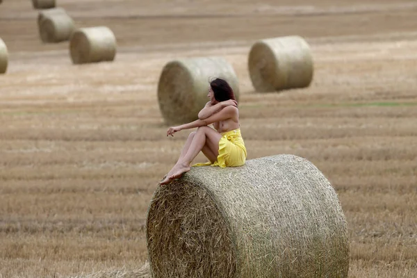 Young woman posing near haystack on the field. Sexy brunette posing outdoors