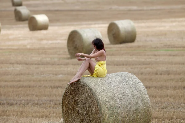 Young woman posing near haystack on the field. Sexy brunette posing outdoors