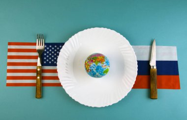 Beyaz bir plaka, mavi bir masanın üzerinde dünyanın bir modeli, yan tarafında bir çatal ve bıçak, Rusya ve Amerika Birleşik Devletleri bayrakları, başkanlık müzakereleri konsepti.