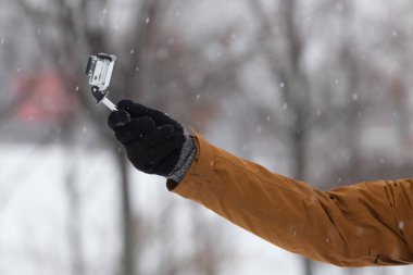 Derin karda küçük kameranın önünde el kamerasıyla çekim yapan bir adam. Doğa, şehir parkında fırtına. Açık hava aktivitesi.