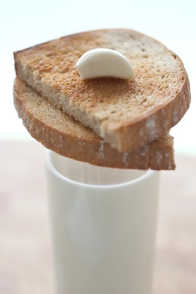 Clavo de ajo sentado en dos rebanadas de pan tostado marrón sobre un delgado vaso de leche — Foto de Stock