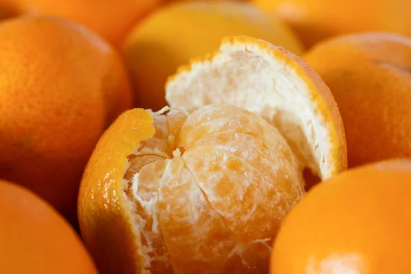 Half peeled tangerine surrounded by unpeeled tangerines — Stock Photo, Image