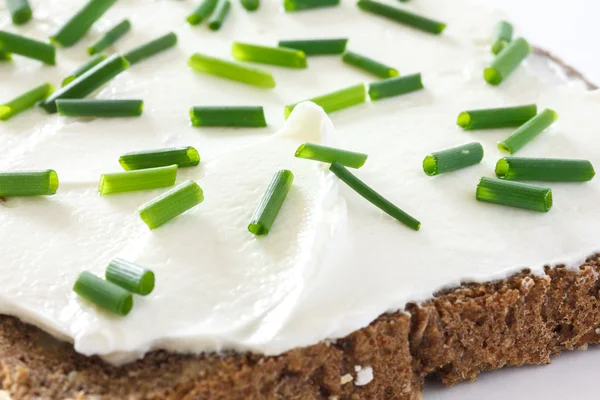 Cut fresh chives on thickly spread cream cheese on dark health bread. — Stock Photo, Image