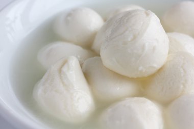 küçük beyaz mozzarella topları beyaz bir tabak sıvı ile.