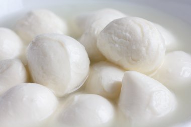 küçük beyaz mozzarella topları beyaz bir tabak sıvı ile.