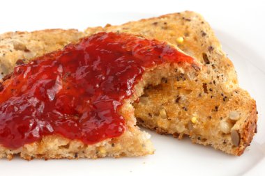 birden çok tohum kepekli ekmek tost ve reçel ile tereyağı sürdüm. eksik ısırmak.