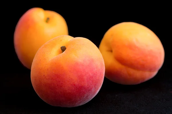 Three beautiful ripe apricots arranged on black. — Stock Photo, Image