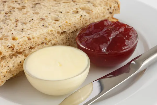 Два ломтика многозернового хлеба с джемом и маслом в тарелках — стоковое фото