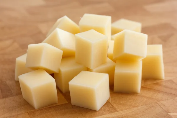 Cubi di formaggio giallo impilati casualmente sul tagliere di legno . — Foto Stock