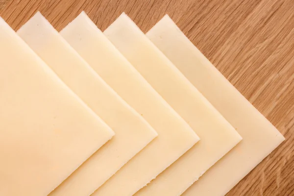 Plakjes gele broodje kaas netjes gerangschikt op een houten oppervlak. schot van bovenaf. — Stockfoto