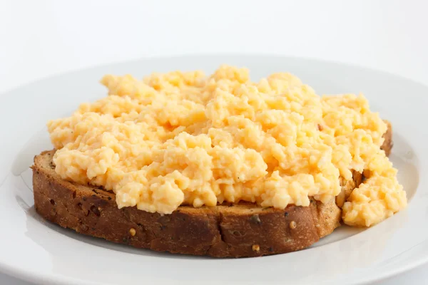 Soft scrambled eggs on brown toast on white plate. — Stock Photo, Image