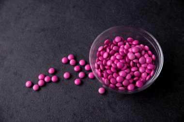 Pembe şeker kaplı çikolata düğmeleri koyu bir tabakta serpiştiriliyor - M & M, Smarties, Srinkles