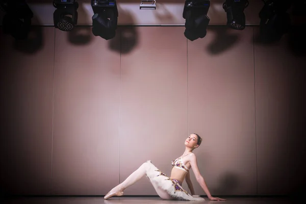 チュチュのスカートの中で若い美しい優雅な白人バレリーナ練習バレエの位置 スタジオの床に座っている古典バレエダンサー — ストック写真