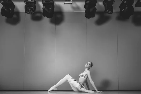 チュチュのスカートの中で若い美しい優雅な白人バレリーナ練習バレエの位置 スタジオの床に座っている古典バレエダンサー — ストック写真