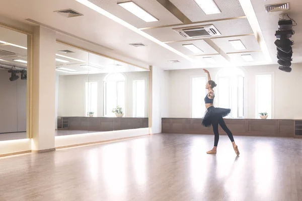 A graceful ballet dancer in a black tutu performs ballet exercises in front of a mirror in the studio