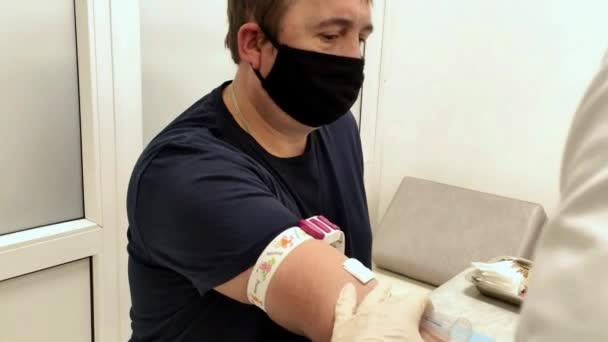 Enfermera toma sangre de una vena de un hombre con una camiseta negra. — Vídeos de Stock