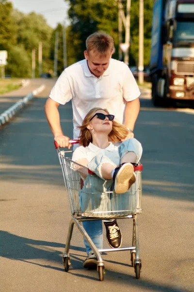 Een mooi jong stel heeft plezier, een man duwt een winkelwagentje, en zijn vriendin zit daar. — Stockfoto