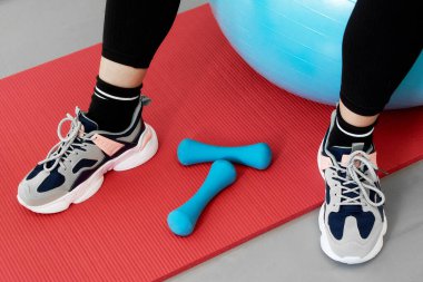 Ayakları kırmızı yoga minderinde mavi bir spor topunun üzerinde oturan bir kadının yakın çekimi..