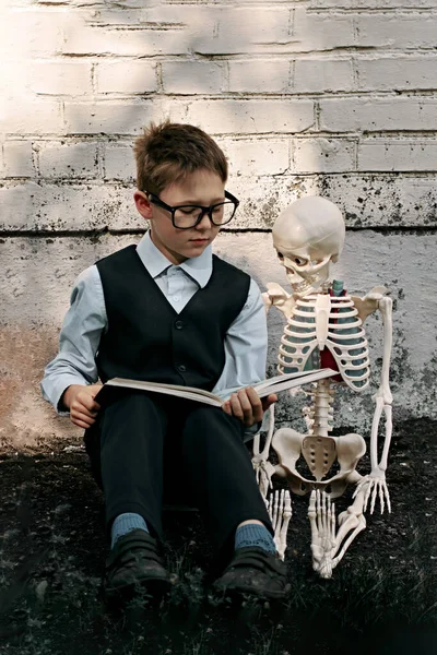 Portré egy iskolás fiúról, aki egy csontvázat ölelget. A test szerkezetének tanulmányozása. — Stock Fotó