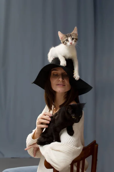 Gatito blanco está sentado en el sombrero con una cabeza de ala grande de una mujer joven. — Foto de Stock