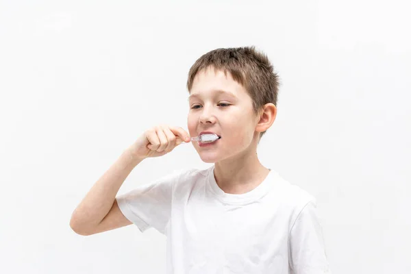 Um rapaz de t-shirt branca está a escovar os dentes na casa de banho.. — Fotografia de Stock