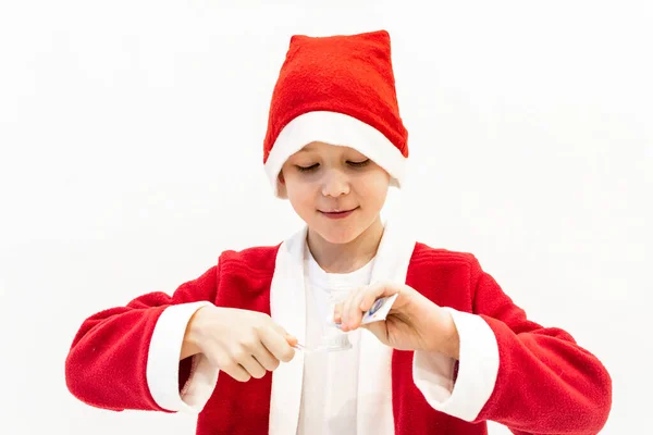 Um menino em um traje de Papai Noel está escovando os dentes no banheiro. — Fotografia de Stock