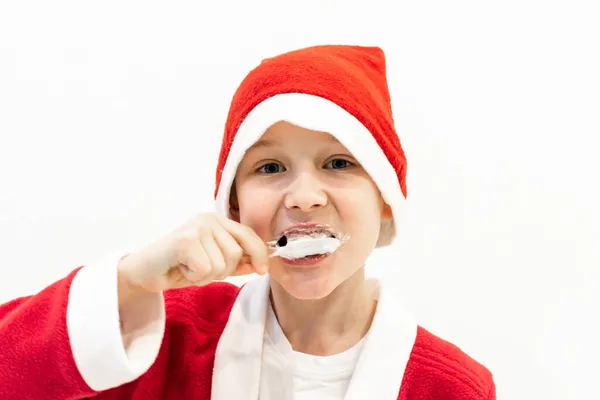 A boy in a Santa costume is brushing his teeth in the bathroom. Stock Picture