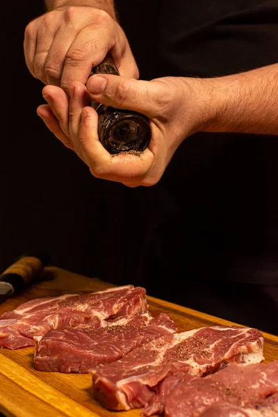 Közelkép a szeletelt húsra borsot szóró kezekről. — Stock Fotó