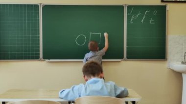 8-9 yaşındaki bir öğrenci tahtaya tebeşirle şekiller çizer.