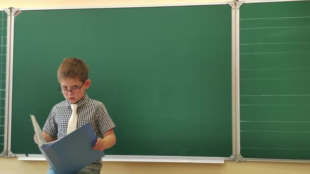 Estudante com óculos lê um livro no quadro negro — Vídeo de Stock
