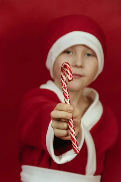 Αγόρι σε ένα κόκκινο κοστούμι Άγιος Βασίλης κρατά γλειφιτζούρια στα χέρια του και χαμόγελα. — Φωτογραφία Αρχείου