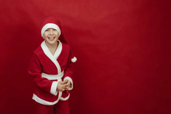 Menino em um traje de Papai Noel vermelho segura pirulitos em suas mãos e sorri. — Fotografia de Stock