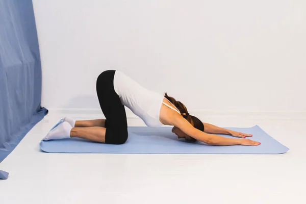 young woman is doing gymnastics on a yoga mat or pilates mat.