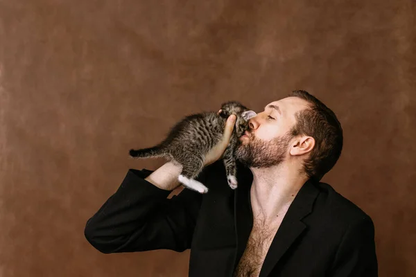 Man leker med en kattunge. Kramar honom och kysser honom Stockbild
